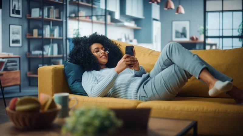 A woman lounging around on a sofa, looking at her phone. Credit: gorodenkoff, via iStock.