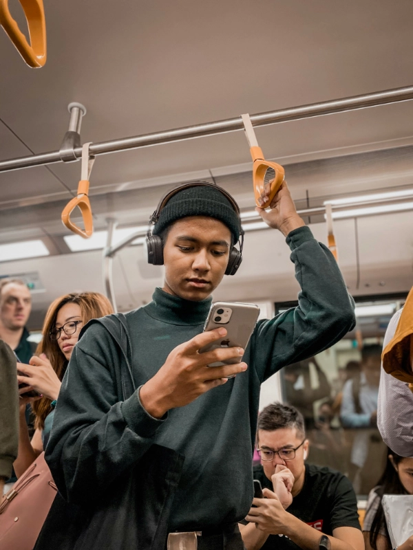 Man in train wearing headphones, holding a smartphone. Credit: Rasheed Kemy, via Unsplash.