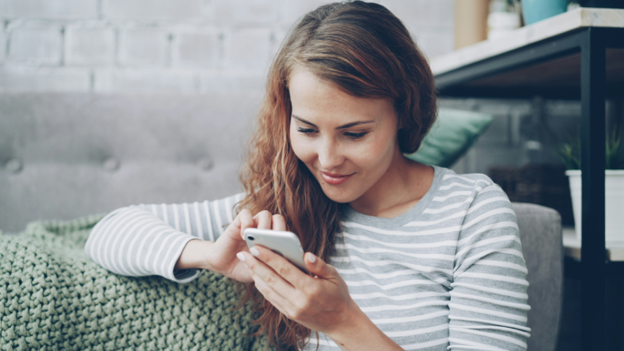 A young woman smiling while looking at her phone. Credit: Vitaly Gariev, via Unsplash.